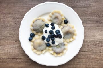 Pierogi z jagodami leśnymi polane śmietanką